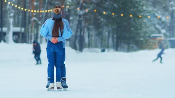 Couple Hugs Standing on Outdoor Skating Rink with Garlands