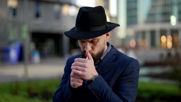 a Bearded and Mustachioed Man in a Hat and a Plaid Jacket Lights a Cigarette Against the Background