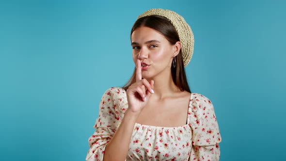 Beautiful Woman in Floral Dress Holding Finger on Her Lips Over Blue Background. Gesture of Shhh