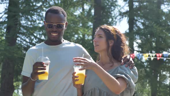 Different Races Couple Walks Drinking Lemonade in Park