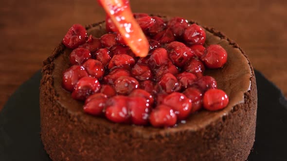 Woman decorates chocolate cheesecake with cherry sauce