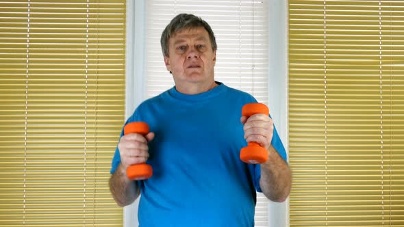 Mature Adult Man with Dumbbells in Hand Runs on Spot at Home Near Window with Blinds