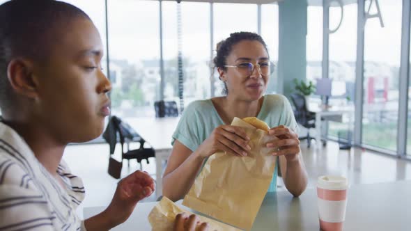 Diverse female creative colleagues eating and talking in workplace canteen