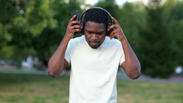 African American Man Putting on Headphones Walks in Park