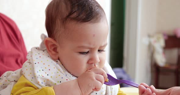 Mother Holds the Baby in Her Arms and Feeds Her Boy with a Spoon