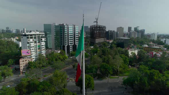 Orbital footage left to right around mexican flag with view of an principle avenue in Mexico City at