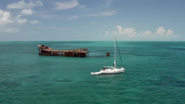 Aerial View of Shipwreck and Sailboat in Ocean Water by Bimini Island, Bahamas. Old Cargo Ship in De