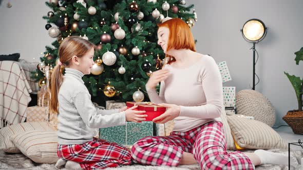 Zoom Out Shot of Happy Little Girl Giving Xmas Gift to Her Grateful Mother Both Sitting Under