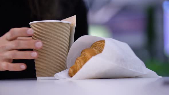 Tasty Fresh Croissants with Coffee in a Paper Cup in Female Hands on Blurred Background