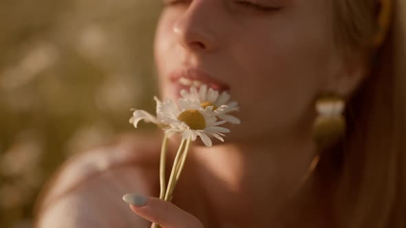 Portrait of a Happy Woman with Camomiles on Field at Sunset