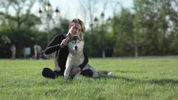 Beautiful Young Woman Playing with Funny Husky Dog Outdoors in Park at Sunset or Sunrise on Green