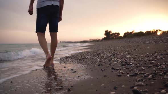 A Slender Elderly Grayhaired Man Slowly Walks Barefoot on a Deserted Beach in the Running Waves in