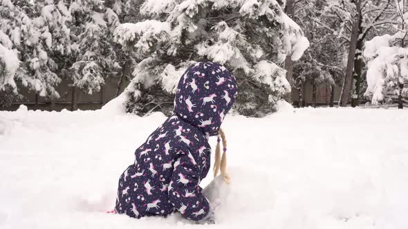 Child Girl Sculpts a Snowman in Winter