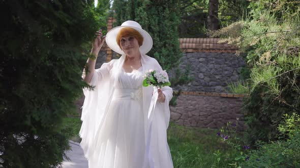 Portrait of Happy Senior Redhead Bride in White Wedding Dress and Straw Hat Smiling Looking at