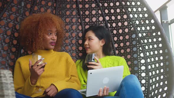 Two Woman Relaxing in the Swing, Best Friends Drinking Red Wine. Multiracial Relationship