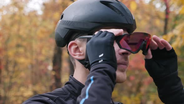 Motivated young cyclist athlete in black helmet puts on sport glasses before workout on bike