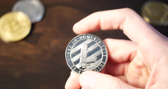 A hand picks up a digital cryptocurrency litecoin and examines it as he thinks about a decentralized