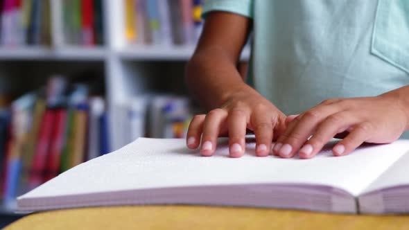 Mid-section of school kid reading a braille book in classroom at school