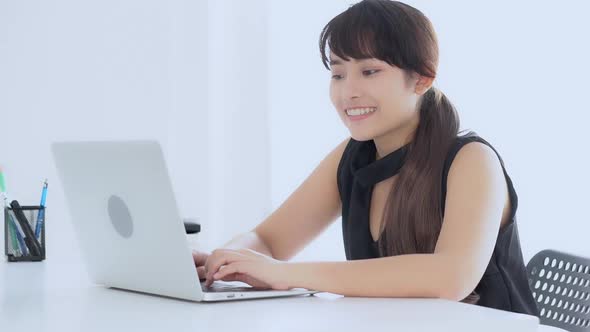 Beautiful young freelance asian woman smiling working and typing on laptop computer at desk office.