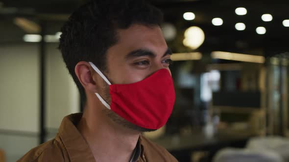 Portrait of a mixed race businessman wearing face mask looking at camera in modern office