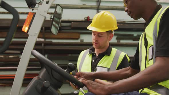 An African American and a Caucasian male factory worker at a factory talking in a warehouse area