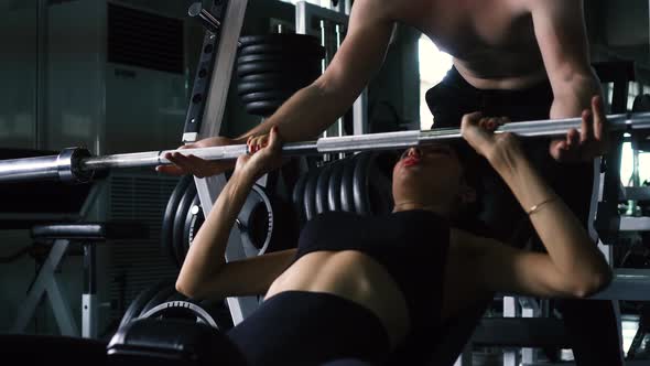 Personal Trainer Helping Woman Bench Press in Gym