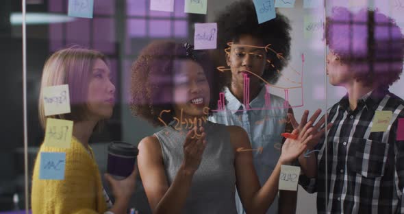 Diverse work colleagues writing and drawing on glass wall having a discussion