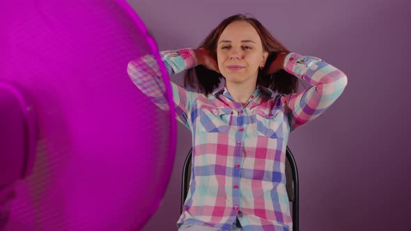 Close Up of Young Woman Sitting on Chair in Front of Fan on Purple Background