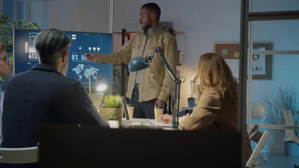 African American Employee Speaking to Diverse Group of Colleagues During Presentation in Dark Office