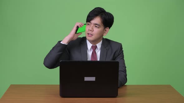 Young Handsome Asian Businessman Working with Laptop Against Green Background