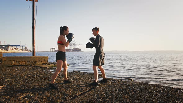 Young Girl in Boxing Gloves and Sport Clothes is Practicing on a Boxing Paw with Her Professional