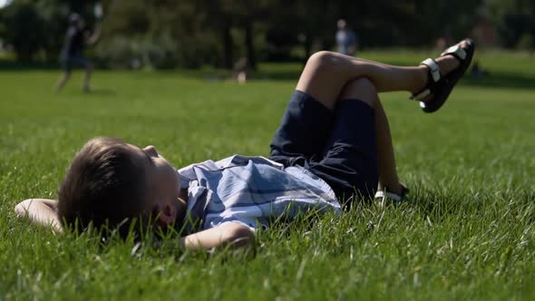 An Attractive Boy Lies in a Park on the Grass Having a Good Mood During the Day in Sunny Weather