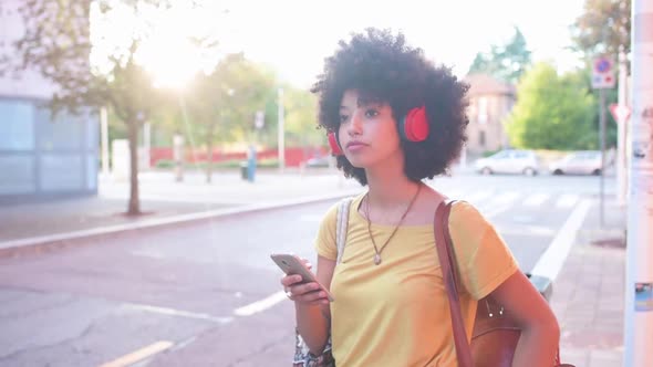 Young woman with headphones using smartphone and waiting at street