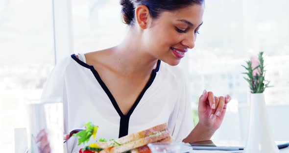 Woman eating lunch and using tablet computer