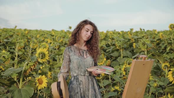 Happy Lady Undresses Hat and Shakes Her Hair at Canvas Among Sunflowers