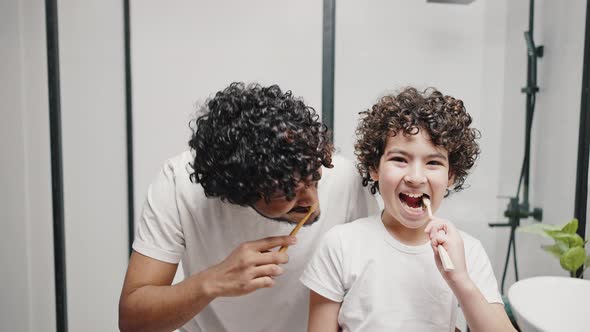 Funny Curlyhaired Brothers Brush Teeth Smiling in Bathroom