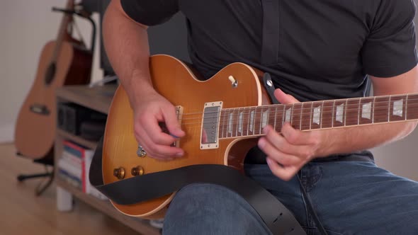 Young man playing expensive guitar on a nice black stool with a second guitar in the background (4K)