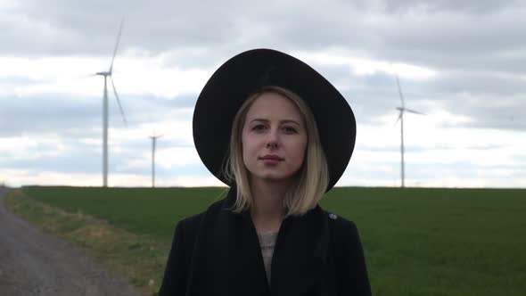 Woman in coat and hat on field with wind turbines on background