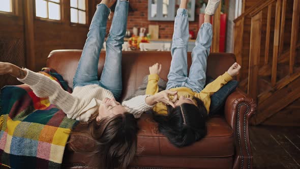 Young Mum and Little Daughter Laughing Laying on Couch with Their Feet Up Tickling Each Other