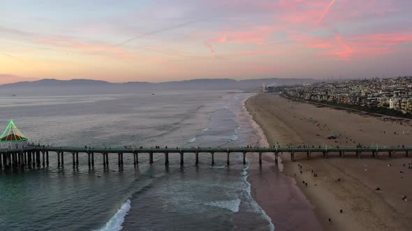 People Walking At Manhattan Beach Pier And Beach At Sunset In California, USA. - aerial