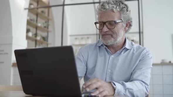 Cheerful Mature Businessman Using Laptop in Co-working Interior