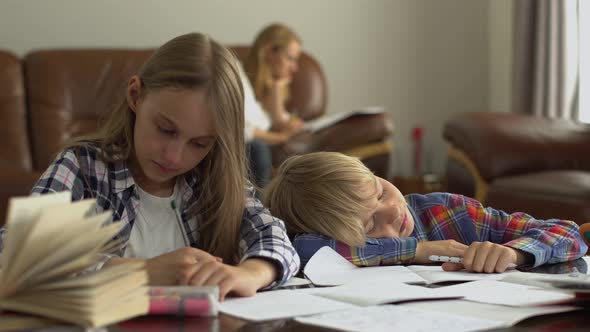 Two Cute Schoolkids Studying at Home in the Foreground While Their Mother Sitting in the Background