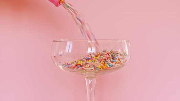 Colorful Candy Confectionery Run Poured Into a Wineglass Glass on Pink Background