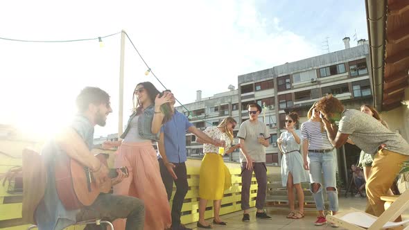 Happy people dancing and playing guitar at the rooftop party on sunny day