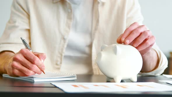 Company financial director in yellow shirt throws silver coin into white piggy bank slot