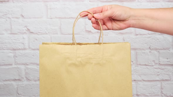 female hand puts brown paper bag with handles for shopping and products