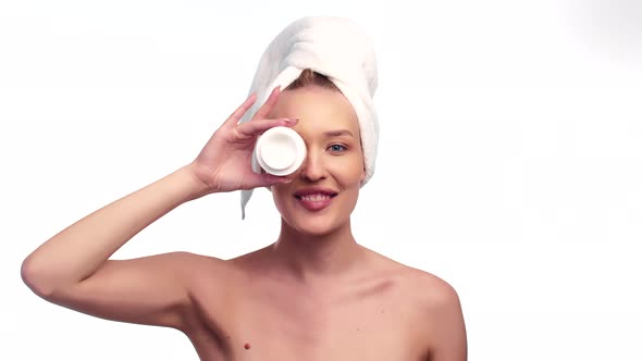 Beautiful Woman with Towel on Head Holds a Jar of Cosmetic Cream Healthy for Skin at Eye Level and