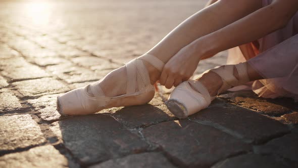 Woman Ties Ribbons of Pointe Shoes Around Leg at Sunrise