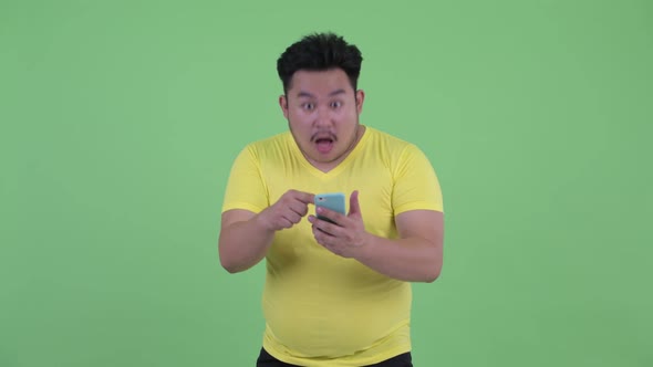 Happy Young Overweight Asian Man Using Phone and Getting Good News