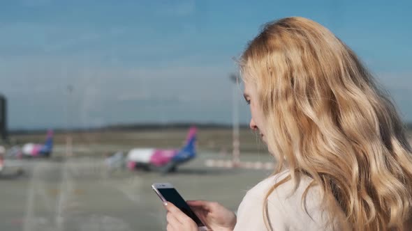 woman uses a smartphone against the background of an airplane